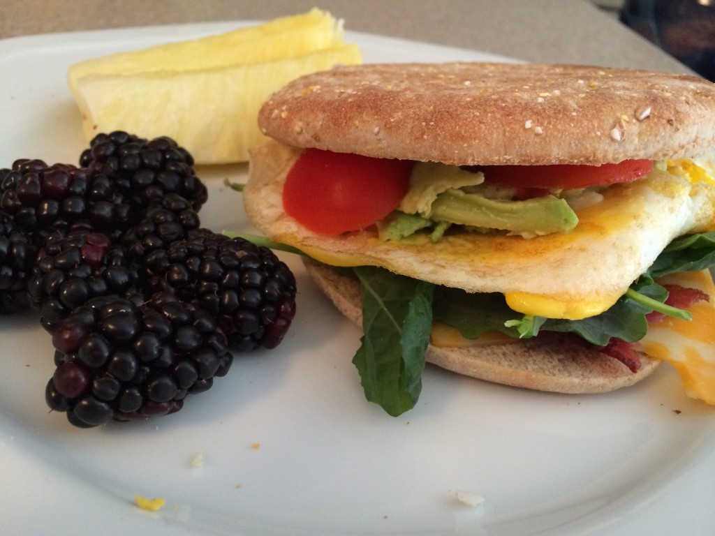 bacon, egg, cheese, avocado, kale, and tomato on a sandwich thin and blackberries and pineapple