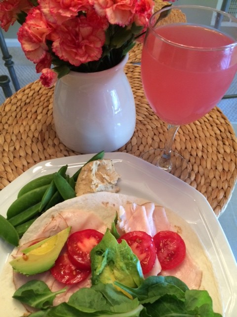 Turkey, avocado, lettuce and tomato in a flour tortilla, some snap peas with hummus and pink lemonade in a wine glass just because